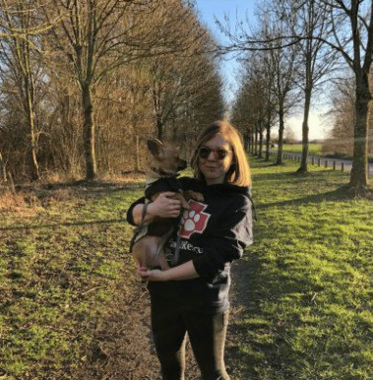 A photo of Paws2Rescue team member Magdalena standing in the beautiful countryside holding a small dog